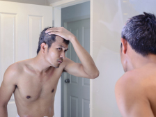 Man worried about gray hair while looking into a mirror.